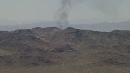 4K aerial stock footage of a column of black smoke rising behind Mojave Desert mountains in San Bernardino County, California Aerial Stock Footage | FG0001_000056