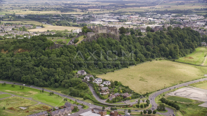 Historic Stirling Castle sitting atop a tree covered hillside, Scotland Aerial Stock Photo AX109_022.0000135F | Axiom Images