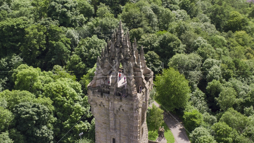 The top of historic Wallace Monument among trees, Stirling, Scotland Aerial Stock Photo AX109_052.0000016F | Axiom Images