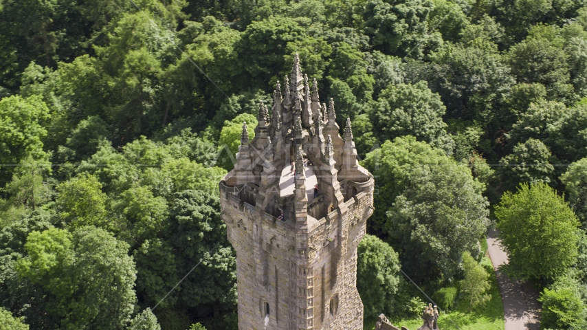 Top of iconic Wallace Monument near trees, Stirling, Scotland Aerial Stock Photo AX109_052.0000110F | Axiom Images