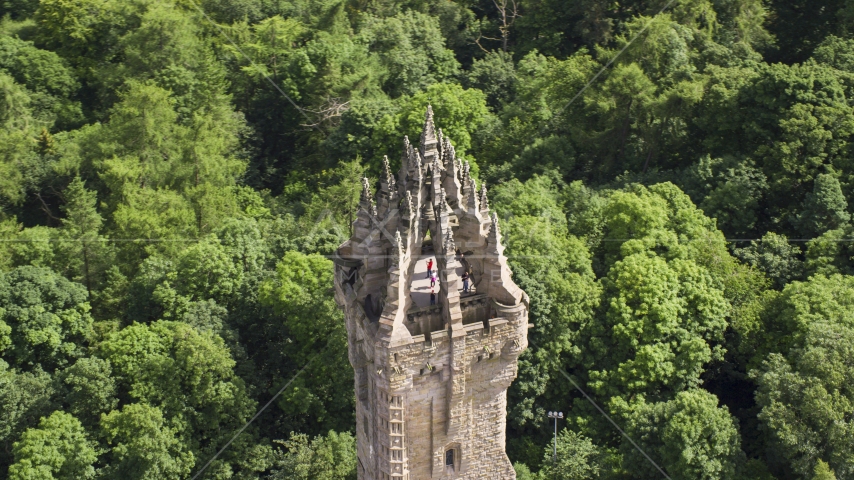 The top of iconic Wallace Monument with tourists, surrounded by trees, Stirling, Scotland Aerial Stock Photo AX109_053.0000000F | Axiom Images