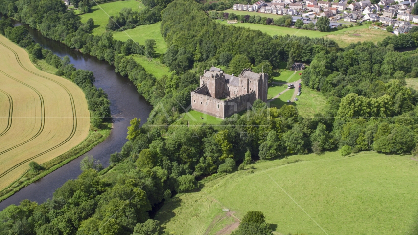 The iconic Doune Castle with trees along a river, Scotland Aerial Stock Photo AX109_074.0000000F | Axiom Images
