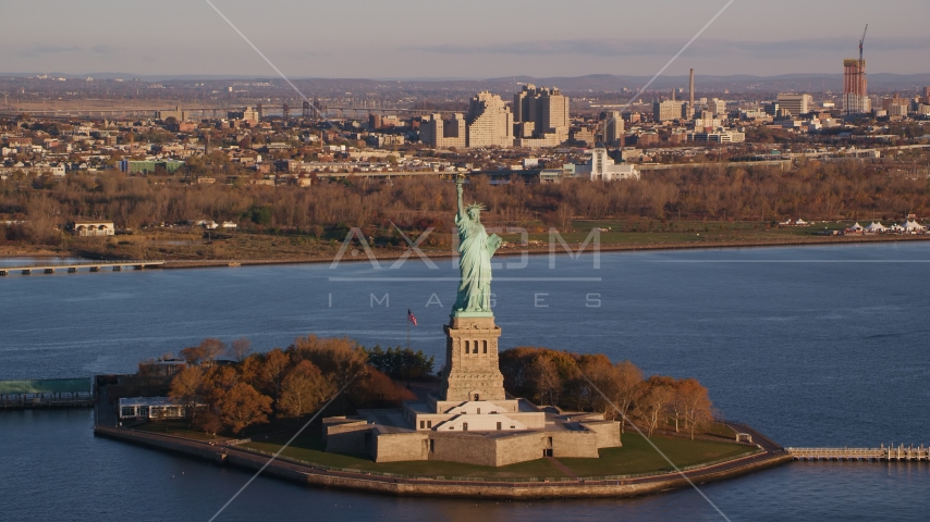 Statue of Liberty at sunrise in New York, with Jersey City in the background Aerial Stock Photo AX118_144.0000175F | Axiom Images