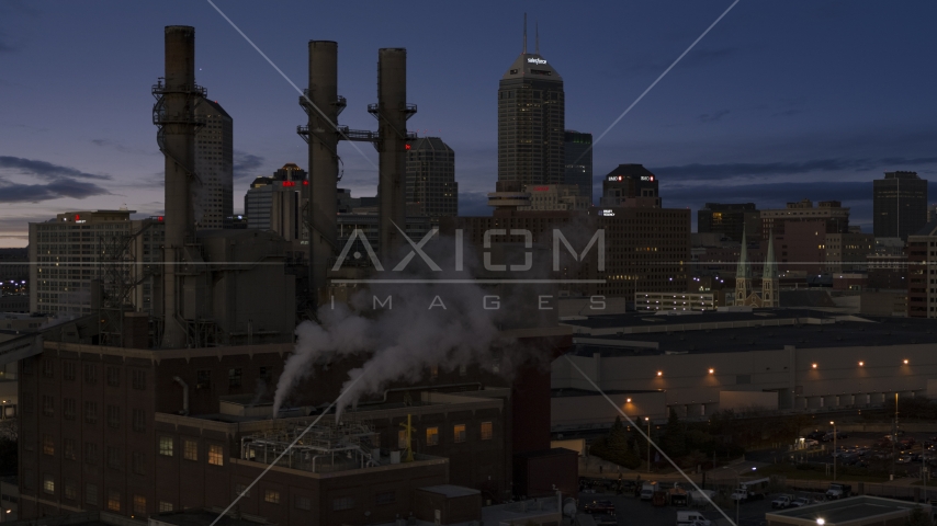 Factory smoke stacks with city skyline in the background at twilight, Downtown Indianapolis, Indiana Aerial Stock Photo DXP001_093_003 | Axiom Images