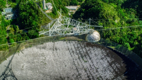 AX101_117.0000306F - Aerial stock photo of Looking downward at the Arecibo Observatory surrounded by trees, Puerto Rico