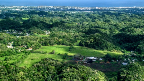 AX101_129.0000000F - Aerial stock photo of Tree covered hills and rural homes near the coast, Arecibo, Puerto Rico