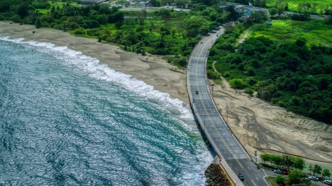 AX101_140.0000000F - Aerial stock photo of Coastal road cutting through trees and over a beach by blue water, Arecibo, Puerto Rico 