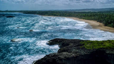 AX101_155.0000000F - Aerial stock photo of Waves rolling toward the beach and tree-lined Caribbean coast, Arecibo, Puerto Rico