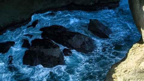 AX101_167.0000171F - Aerial stock photo of Churning water and rocks in a coastal sea cave, Arecibo, Puerto Rico