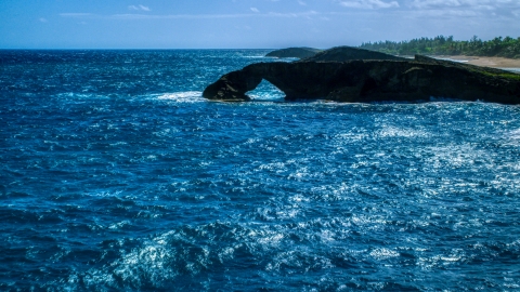 AX101_168.0000129F - Aerial stock photo of An arched rock formation in crystal blue water, Arecibo, Puerto Rico