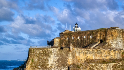 AX104_012.0000023F - Aerial stock photo of The steep walls and lighthouse of the Fort San Felipe del Morro, Old San Juan, sunset