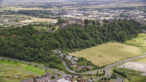 AX109_022.0000135F - Aerial stock photo of Historic Stirling Castle sitting atop a tree covered hillside, Scotland