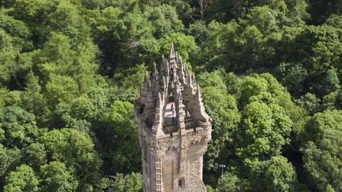 AX109_053.0000000F - Aerial stock photo of The top of iconic Wallace Monument with tourists, surrounded by trees, Stirling, Scotland