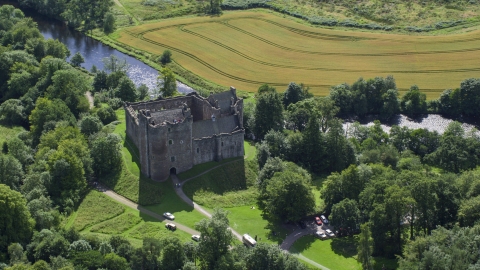 AX109_067.0000164F - Aerial stock photo of Riverfront Doune Castle with trees, Scotland