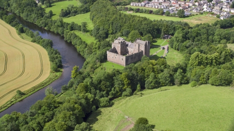 AX109_074.0000000F - Aerial stock photo of The iconic Doune Castle with trees along a river, Scotland