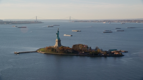 AX118_216.0000172F - Aerial stock photo of Statue of Liberty and barges in New York Bay at sunrise in New York