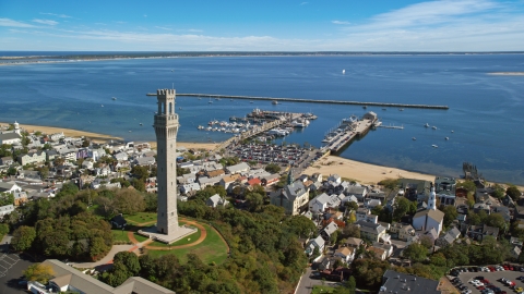 AX143_228.0000028 - Aerial stock photo of The Pilgrim Monument in a small coastal town with a view of piers, Provincetown, Massachusetts