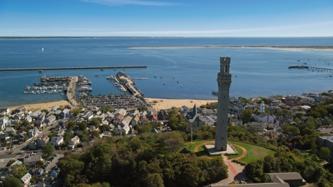 AX143_228.0000285 - Aerial stock photo of The Pilgrim Monument and small coastal town with a view of piers and the bay, Provincetown, Massachusetts