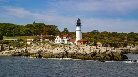 AX147_316.0000190 - Aerial stock photo of The Portland Head Light on a rocky shore, seen from the ocean in autumn, Cape Elizabeth, Maine