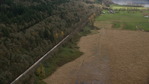 AX153_178.0000352F - Aerial stock photo of A train traveling by fields and water in Washougal, Washington