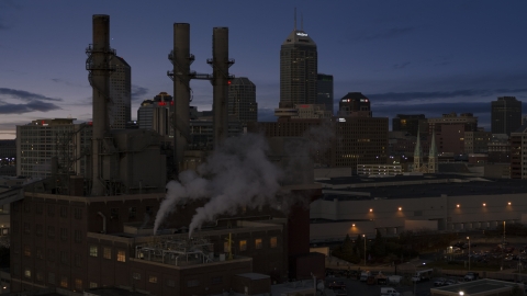 DXP001_093_003 - Aerial stock photo of Factory smoke stacks with city skyline in the background at twilight, Downtown Indianapolis, Indiana