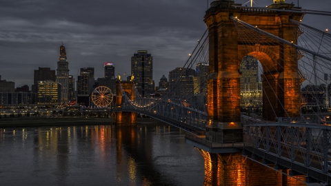 DXP001_098_0003 - Aerial stock photo of The city skyline behind Roebling Bridge lit up at twilight, seen from Ohio River, Downtown Cincinnati, Ohio
