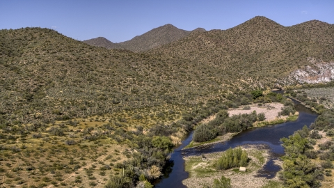 DXP002_141_0024 - Aerial stock photo of A shallow river bordered by desert hills with cactus