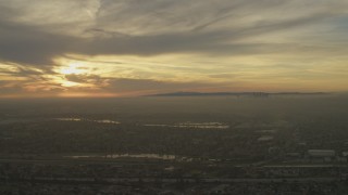 AF0001_000980 - 5K aerial stock footage of setting sun behind clouds and Downtown Los Angeles skyline seen from Pico Rivera, California
