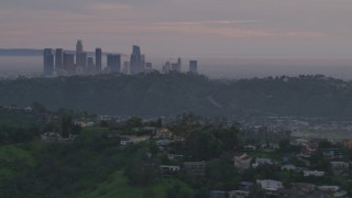 AF0001_001000 - 5K aerial stock footage of Downtown Los Angeles skyline seen while flying by hillside homes at twilight, California