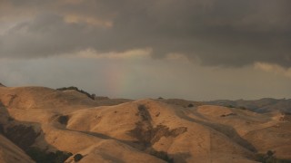 AF0001_001033 - 8K aerial stock footage of a rainbow behind brown mountains at sunset in Northern California