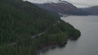 AK0001_0498 - 4K aerial stock footage flying along wooded shoreline and forest road, approaching Whittier, Alaska