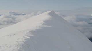 AK0001_0530 - 4K aerial stock footage flying over snowy summit, revealing thick clouds, Kenai Mountains, Alaska