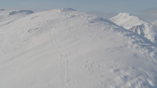 AK0001_0540 - 4K aerial stock footage flying up snowy slope, reveal mountain range below, Kenai Mountains, Alaska