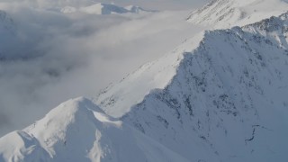 AK0001_0541 - 4K aerial stock footage descending a snowy ridge, approaching low clouds, Kenai Mountains, Alaska