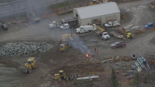 AK0001_0654 - 4K aerial stock footage orbiting burning wood and a bulldozer dumping gravel in a quarry, Chugiak, Alaska
