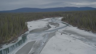 AK0001_0902 - 4K aerial stock footage fly over icy, snow covered river, ascend to show forest during winter, Tazlina River Valley, Alaska
