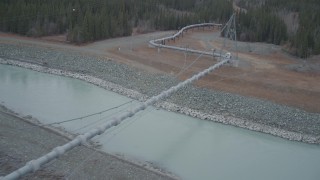 AK0001_1009 - 4K aerial stock footage follow pipeline spanning Tazlina River during winter, Trans-Alaska Pipeline, Alaska