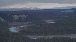 AK0001_1024 - 4K aerial stock footage the Tazlina River at bottom of forested gorge, snowy mountains in the background, Alaska