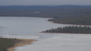 AK0001_1032 - 4K aerial stock footage flying by ice covered Sucker Lake surrounded by forest, Alaska