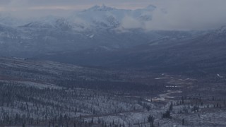 AK0001_1056 - 4K aerial stock footage snow covered, forested hills beneath low clouds, Alaskan Wilderness