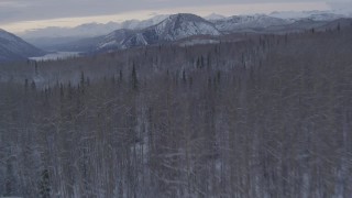 AK0001_1090 - 4K aerial stock footage flying over snow covered, wooded hills toward Matanuska River Valley, Alaska