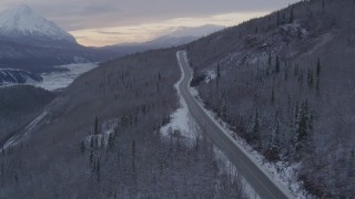 AK0001_1100 - 4K aerial stock footage follow Glenn Highway, snow covered, wooded hills, Sutton, Alaska, twilight