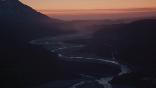 AK0001_1115 - 4K aerial stock footage descending toward a highway and river in the snow covered Matanuska River Valley at sunset, Alaska
