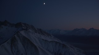 AK0001_1139 - 4K stock footage aerial video the moon over snowy Chugach Mountains, tilt down to valley, Alaska, night
