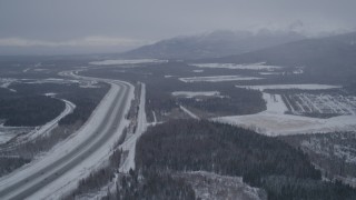 AK0001_1155 - 4K aerial stock footage flying beside snow covered Glenn Highway, Fort Richardson, Anchorage, Alaska