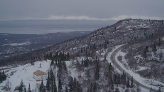 AK0001_1166 - 4K aerial stock footage flying over a home in snow covered wooded hills near Eagle River, Alaska