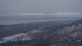 AK0001_1167 - 4K aerial stock footage over snowy, wooded slope, Chugach Mountains revealing Chugiak, Alaska