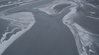 AK0001_1250 - 4K aerial stock footage following a river with snow blowing off the shore, Knik River Valley, Alaska