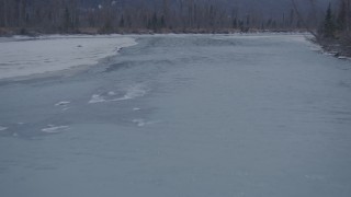 AK0001_1297 - 4K aerial stock footage flying over icy river between snow covered shore, Knik River Valley, Alaska