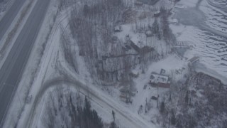 AK0001_1310 - 4K aerial stock footage flying over frozen lake, snowy houses, reveal Glenn Highway, Eagle River, Alaska